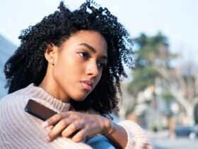 Young BIPOC woman holding phone. Discover how to set boundaries and take back your power.