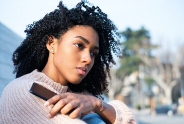 Young BIPOC woman holding phone. Discover how to set boundaries and take back your power.