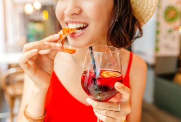 Happy woman eating seafood shrimp and drinking sangria