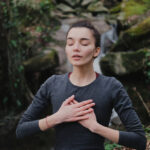 Young woman practicing breathing yoga pranayama outdoors in moss forest