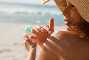 Young woman applying sunscreen on her shoulder while sitting on the beach