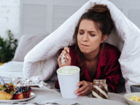 Stressed woman hiding under blanket eating junk food. Learn 3 ways to stop stress eating.