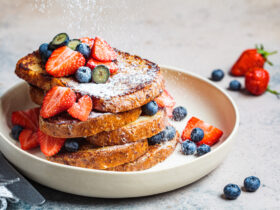 pile of french toast on a white plate with strawberries, blueberries, and powdered sugar