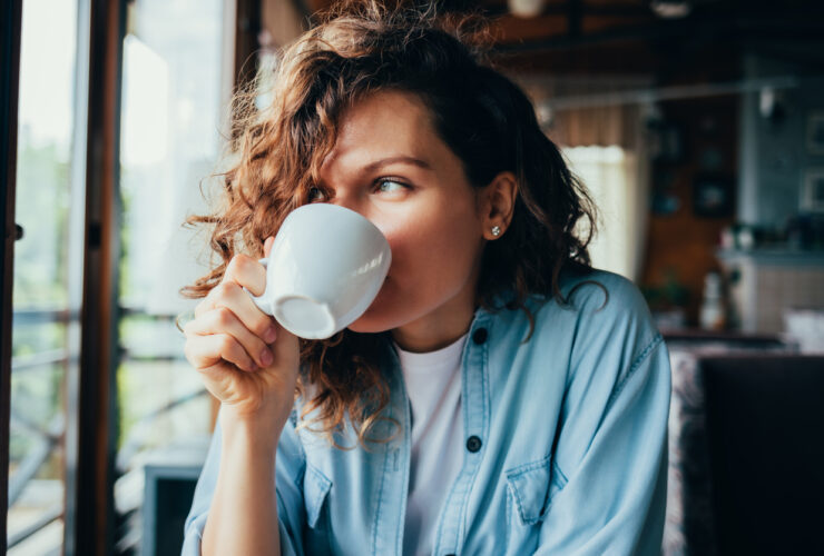 a woman with curly brown hair drinks a beverage out of a coffee cup