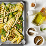 Grilled zucchini and squash slices on a sheet pan with olive oil and lemon slices