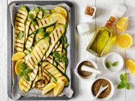 Grilled zucchini and squash slices on a sheet pan with olive oil and lemon slices