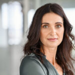 Beautiful hispanic woman in her 40s with brown hair and green shirt wondering how long perimenopause will last.