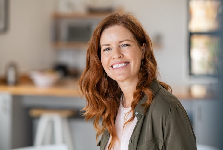 Beautiful woman in her 40s with red hair and a green jacket smiling. Learn when to take progesterone for perimenopause at GloWellmag.com